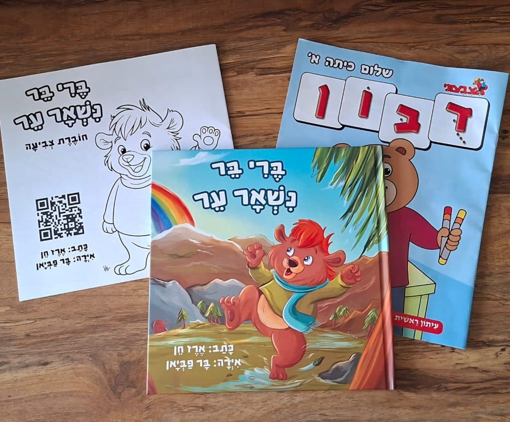 צילום של ספר הילדים "ברי בר נשאר ער" מאת ארז חן, מונח על שולחן לצד חוברת נוספת מסדרת אצבעוני, עם איורים צבעוניים המדגישים את המסר של אהבה וקבלה.